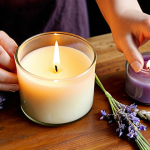 ** "A close-up, warm-toned photograph of hands engaged in the process of making handmade scented candles. The scene features a delicate pour of melted natural soy wax into an elegant glass container, with various bottles of essential oils (like lavender and lemongrass) and dried botanical elements scattered artistically on a wooden surface. Soft, diffused natural light illuminates the crafting area, emphasizing the mindful, therapeutic, and natural aspects of the DIY candle-making process."

2.  **Prompt for